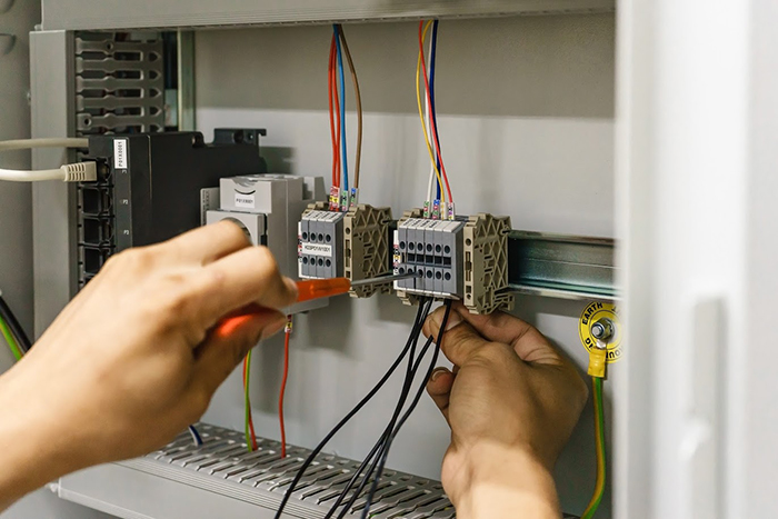 Electrician with a screwdriver macro connect wires on the background of electrical cabinet with relays and terminal blocks.